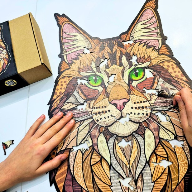 Układanie puzzli na stole jako relaksujące hobby dla dorosłych i starszych dzieci, Osoba układająca puzzle drewniane Leśny Kot - widać ręce i unikalne kształty elementów.